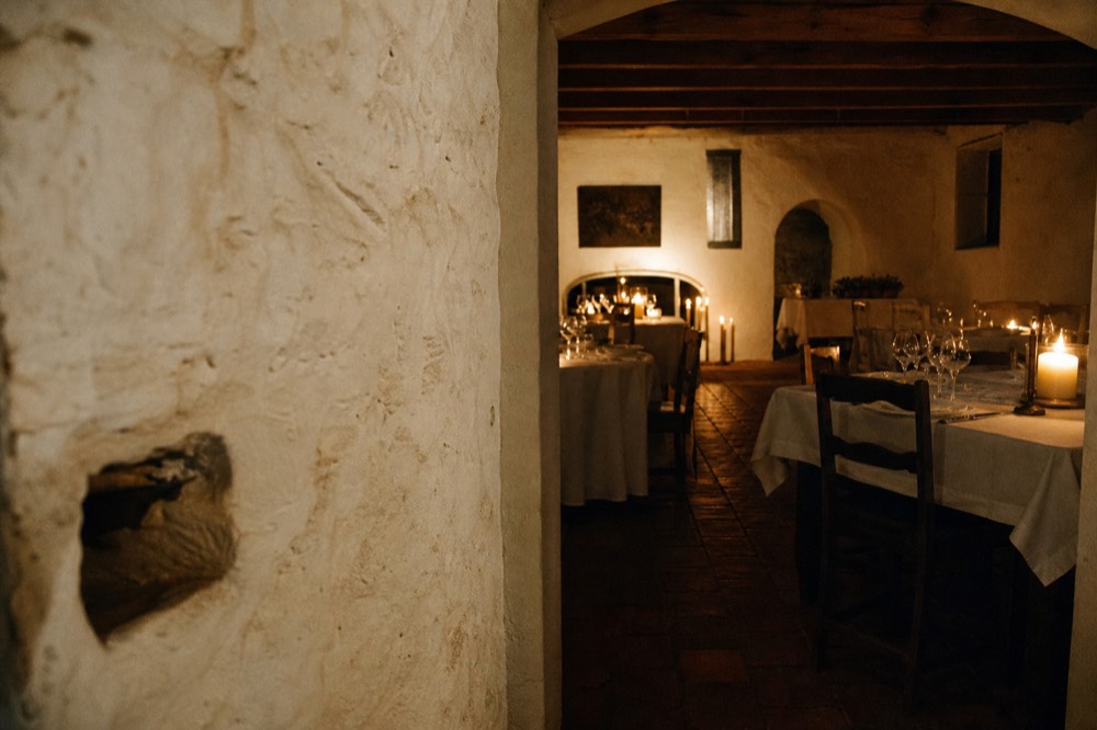 An old stone cellar interior converted to a candlelit dining room with thick whitewashed walls and set tables, warm low light, no people, no text, no signage
